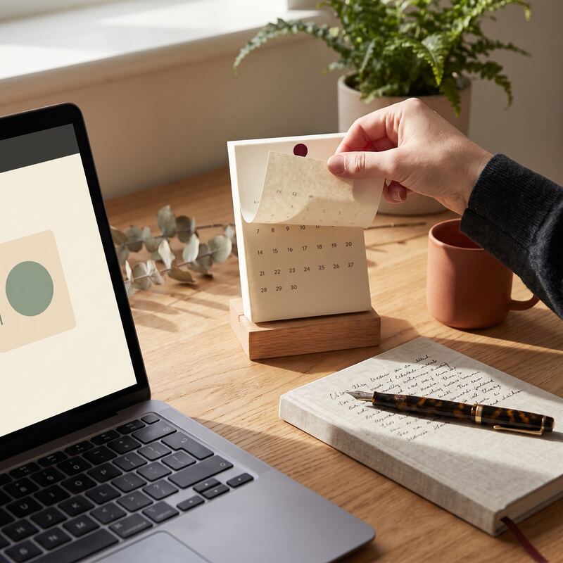 Hand turning a desk calendar page beside a laptop reminder, keeping a monthly API key rotation routine on schedule Hand turning a desk calendar page beside a laptop reminder, keeping a monthly API key rotation routine on schedule
